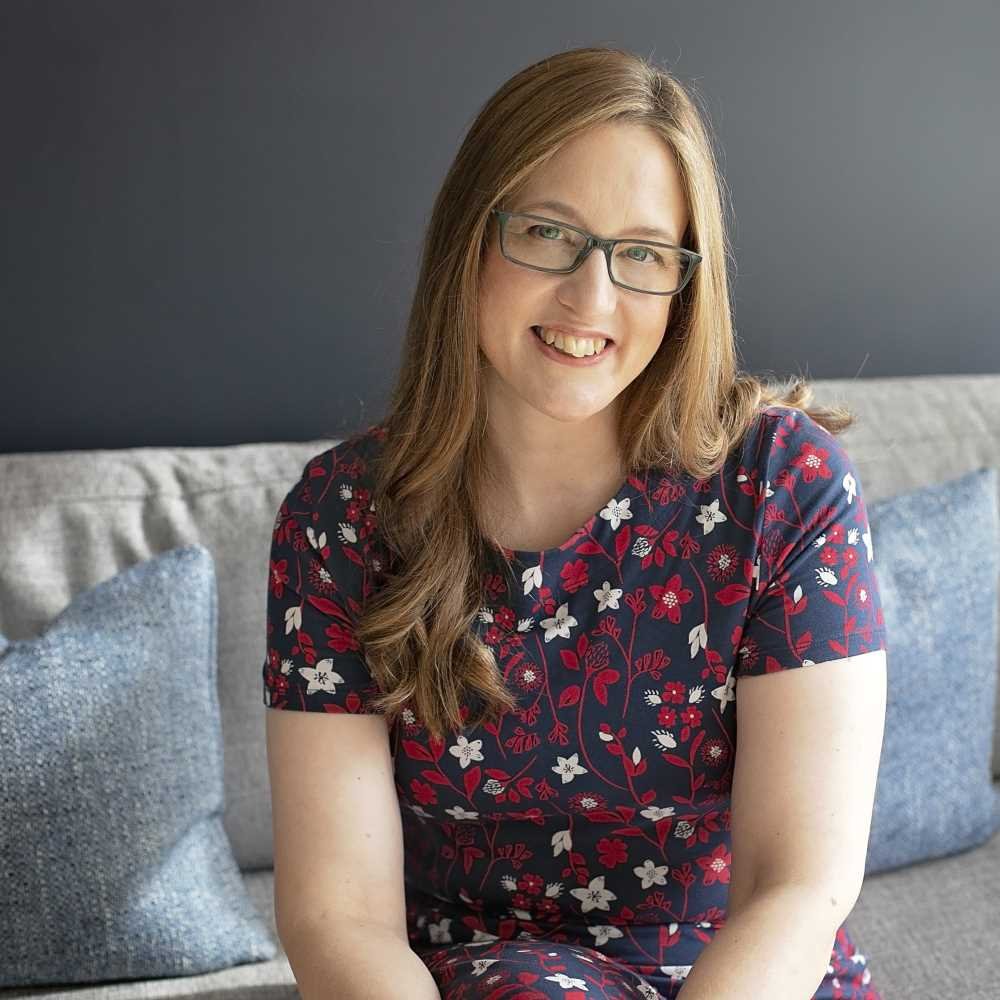 Liz sat on a pale sofa, smiling at the camera